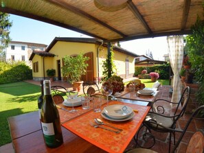 An outdoor dining area with a table set for two, a bottle of wine, and a garden view. - La Capannella by Interhome (Capannori)