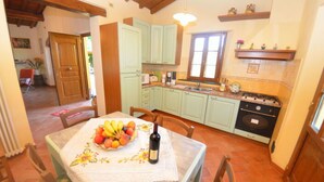A kitchen with light green cabinets, a stove, and a dining table with a fruit bowl and wine bottle. - La Capannella by Interhome (Capannori)