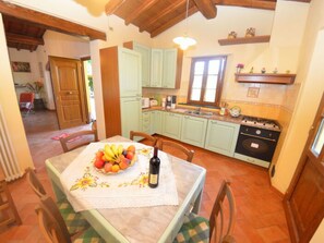 A kitchen with light green cabinets, a stove, and a dining table with a fruit bowl and wine bottle. - La Capannella by Interhome (Capannori)