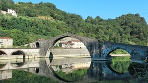 A stone bridge over a calm river with a reflection, surrounded by lush greenery and buildings. - Il Molino by Interhome (Bagni di Lucca)