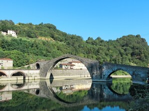 A stone bridge over a calm river with a reflection, surrounded by lush greenery and buildings. - Il Molino by Interhome (Bagni di Lucca)