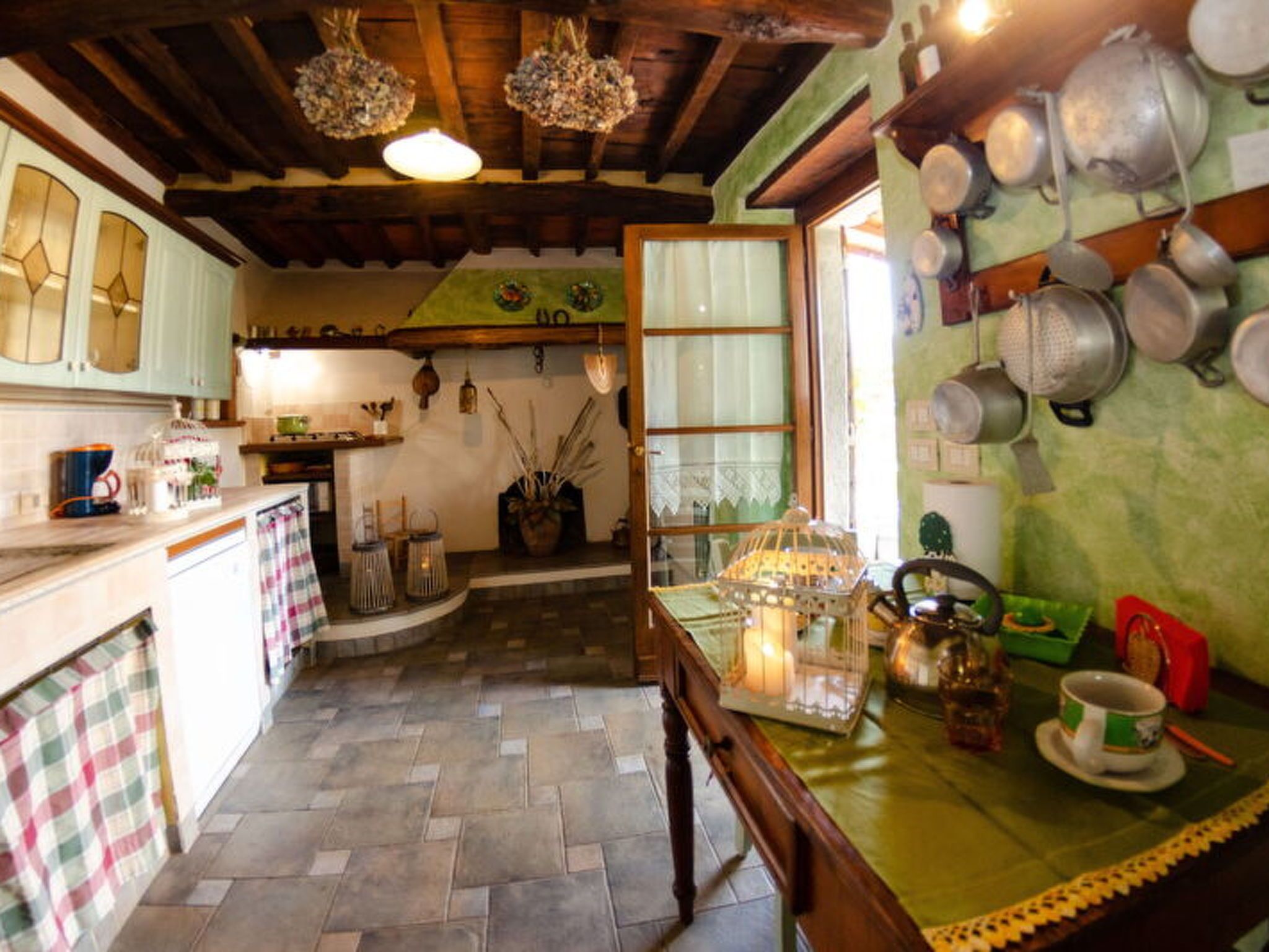 Una cucina rustica con travi in legno, pavimento in pietra e diversi utensili da cucina appesi alle pareti.