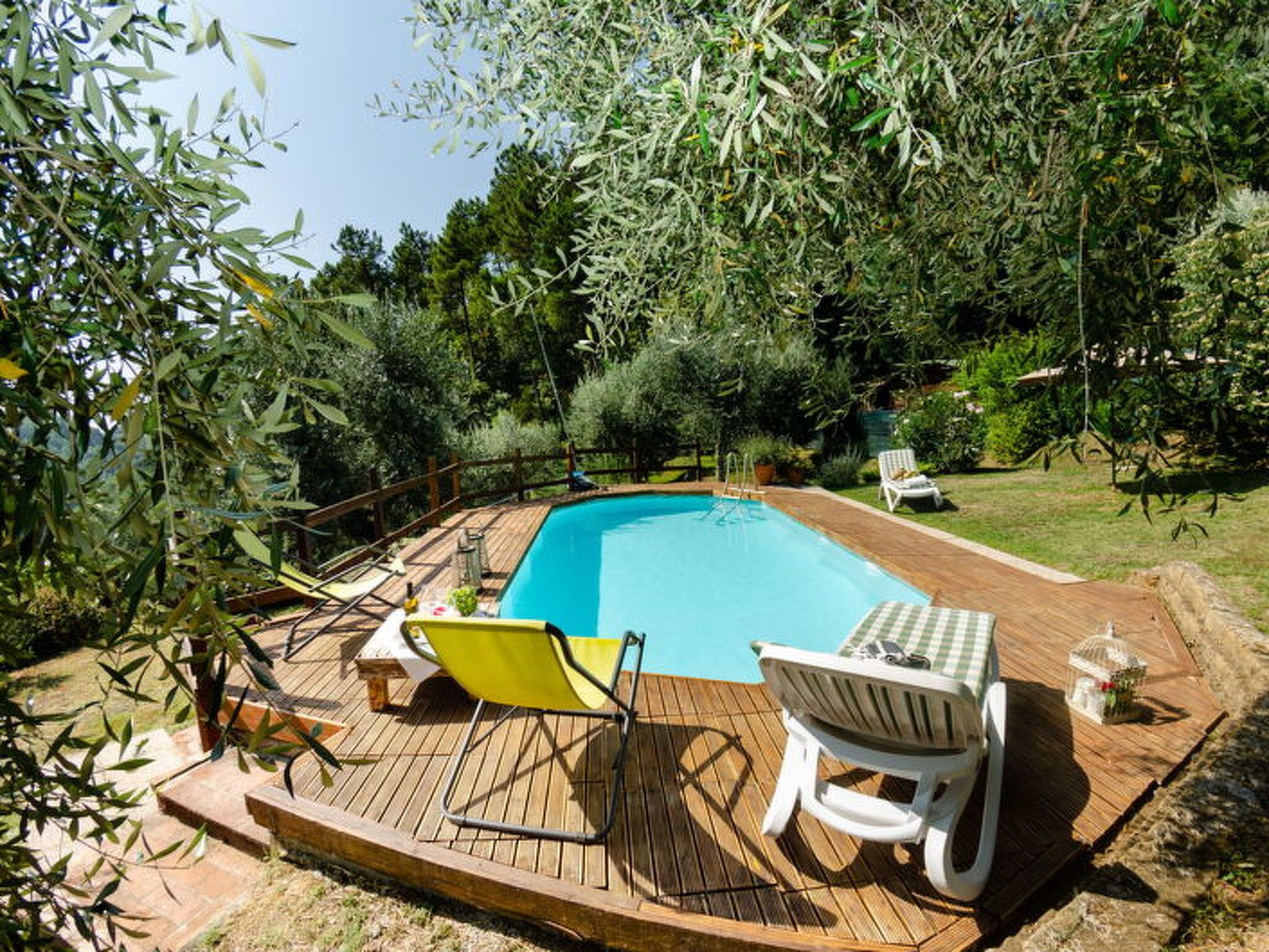 Une piscine avec une terrasse en bois, deux chaises longues et une petite table.