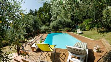Une piscine avec une terrasse en bois, deux chaises longues et une petite table.