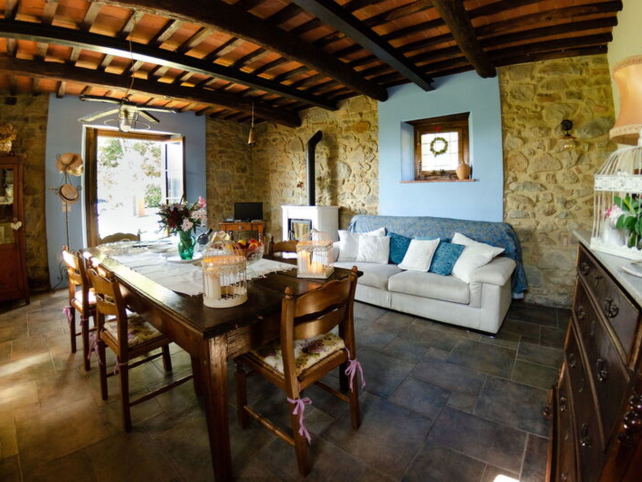 Un'area pranzo rustica con un tavolo e sedie in legno, un muro in pietra e un divano bianco.