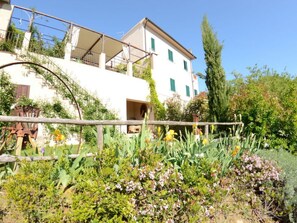 Ein weißes Gebäude mit Balkon, umgeben von Grünpflanzen und Blumen.
