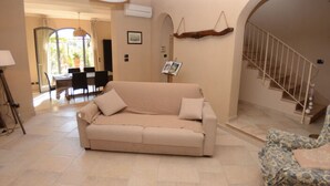 A living room with a sofa, a patterned armchair, a staircase, and a dining area with chairs and a table. - Al Colle Di Lari by Interhome (Lari)