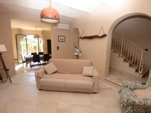 Ein Wohnzimmer mit Sofa, einem gemusterten Sessel, einer Treppe und einem Essbereich mit Stühlen und Tisch.