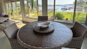 Un tavolo rotondo da pranzo con sedie in vimini, ampie finestre con vista su un lago e un soffitto con travi in legno.