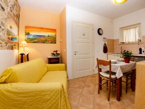 Ein gemütlicher Wohnraum mit gelbem Sofa, Esstisch mit Stühlen, Küchenzeile und einem Bild an der Wand.
