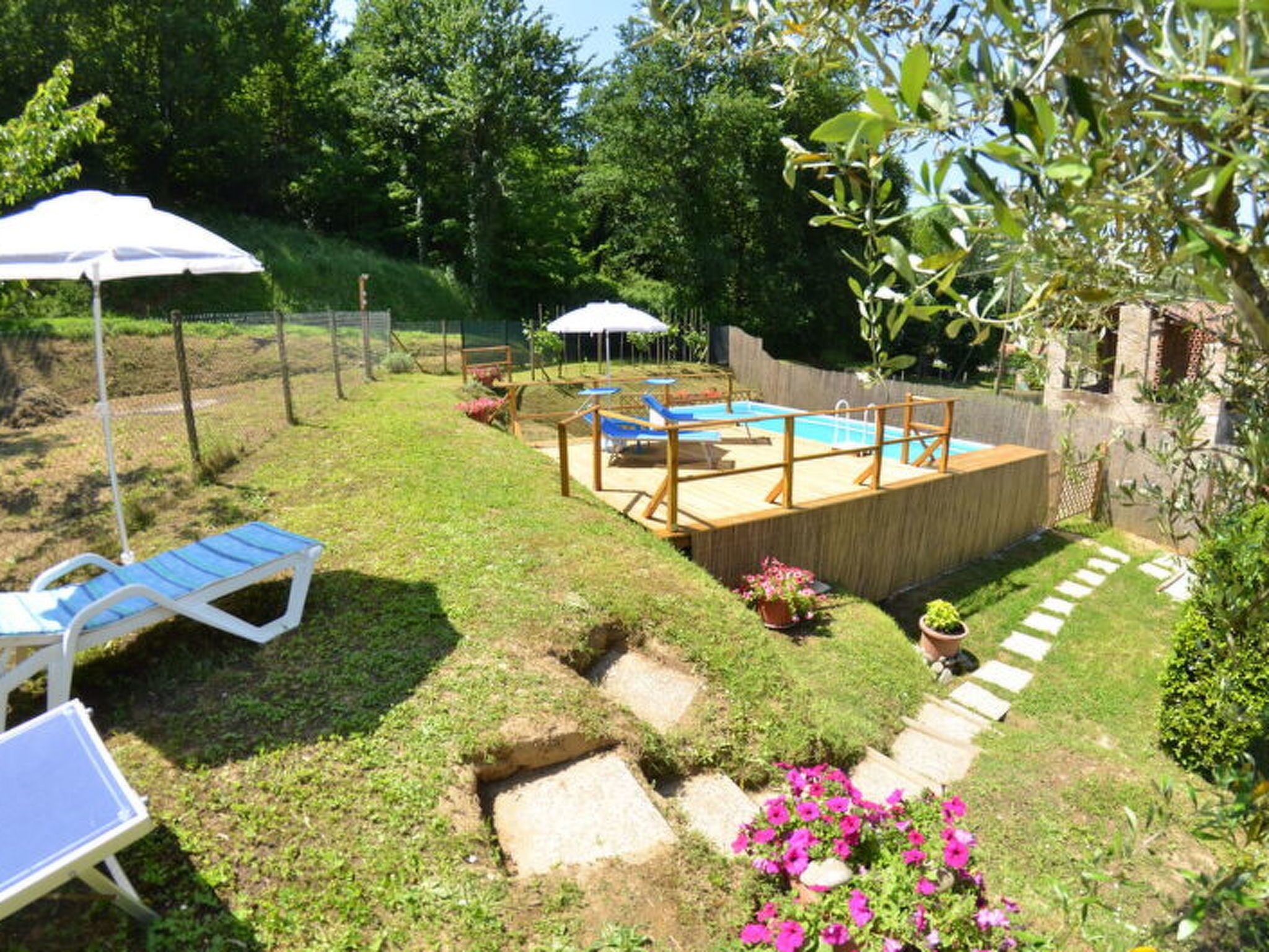 A backyard with a swimming pool, a wooden deck, and a grassy area with a stone pathway.