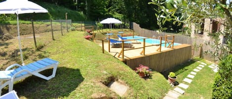 A backyard with a swimming pool, a wooden deck, and a grassy area with a stone pathway.
