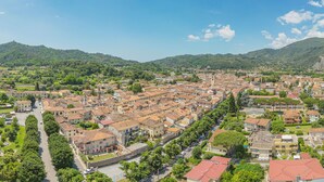 Uma cidade com edifícios históricos, uma rua central e colinas ao redor.