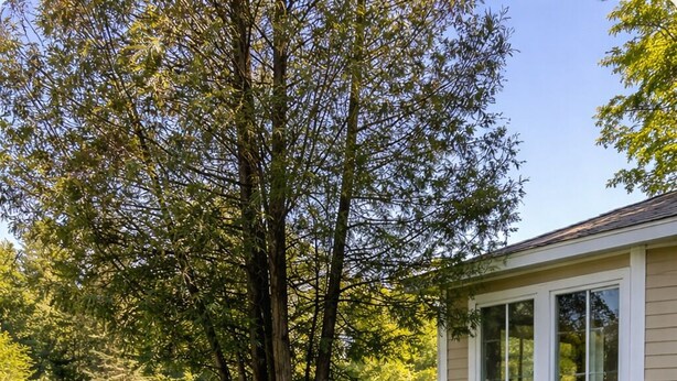 Uma casa com alicerce de pedra, um pequeno alpendre e um gramado com um lago.