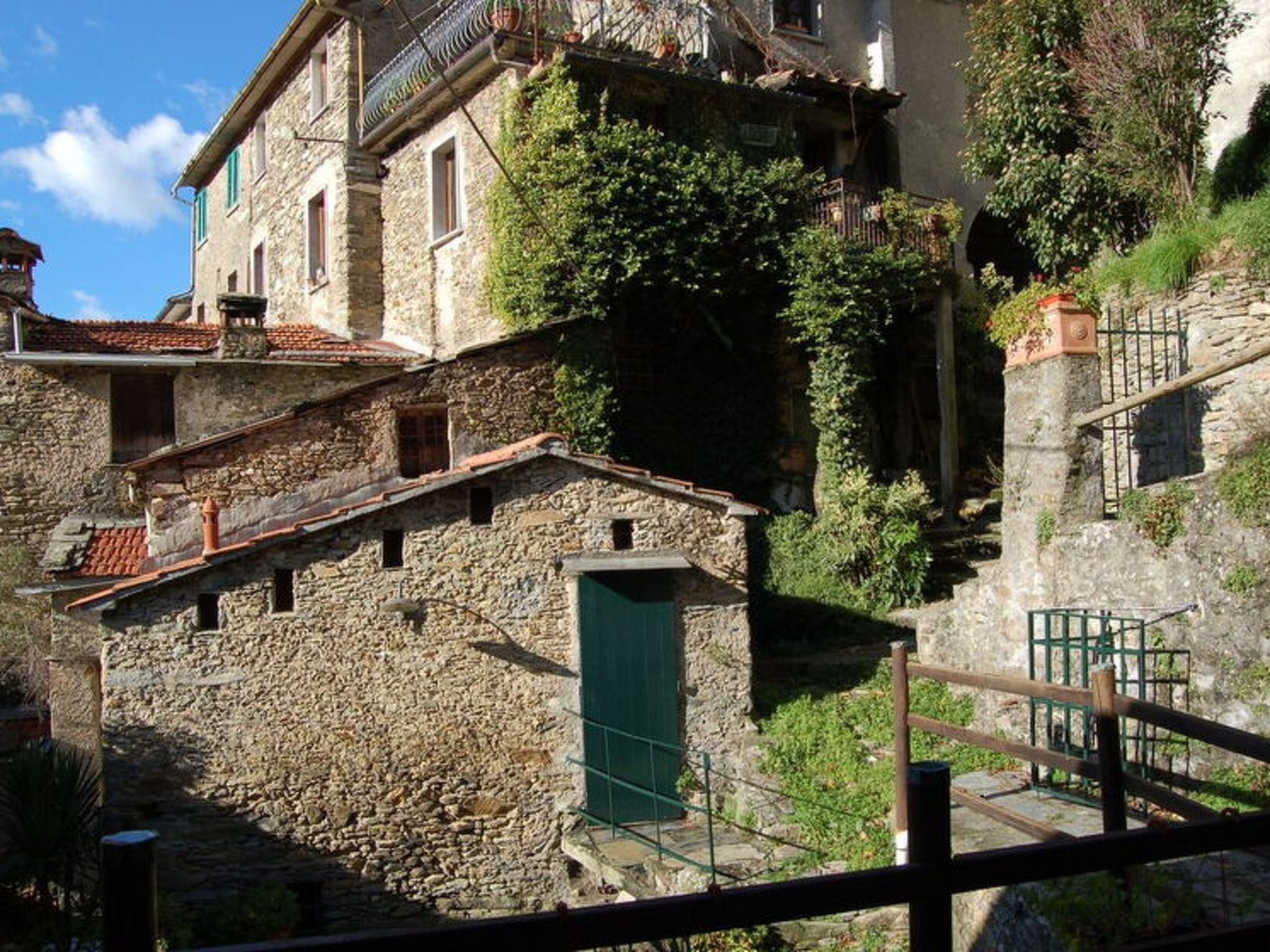 A stone building with a green door, a staircase, and a balcony.