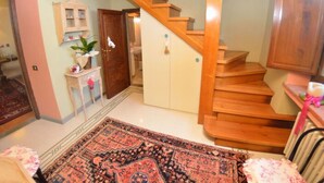 Eine Treppe führt zu einer zweiten Etage, eine Holztür, ein kleiner Tisch mit einer Pflanze und ein gemustertes Teppich.
