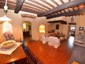 A rustic interior with exposed wooden beams, a dining area with a table set for two, and a kitchen visible in the background. - Villa Sandra Ortensia by Interhome (Casalguidi)