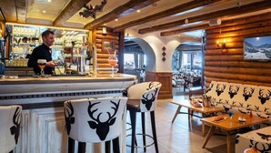 A bar area with stools, a bar counter, and a bartender. There are tables and chairs in the seating area. - Les Campanules Hotel Restaurant (Tignes)