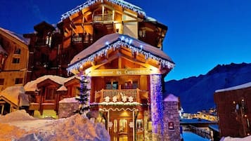 Un immeuble à plusieurs étages doté d’un balcon, entouré d’un paysage enneigé et agrémenté d’une enseigne lumineuse.