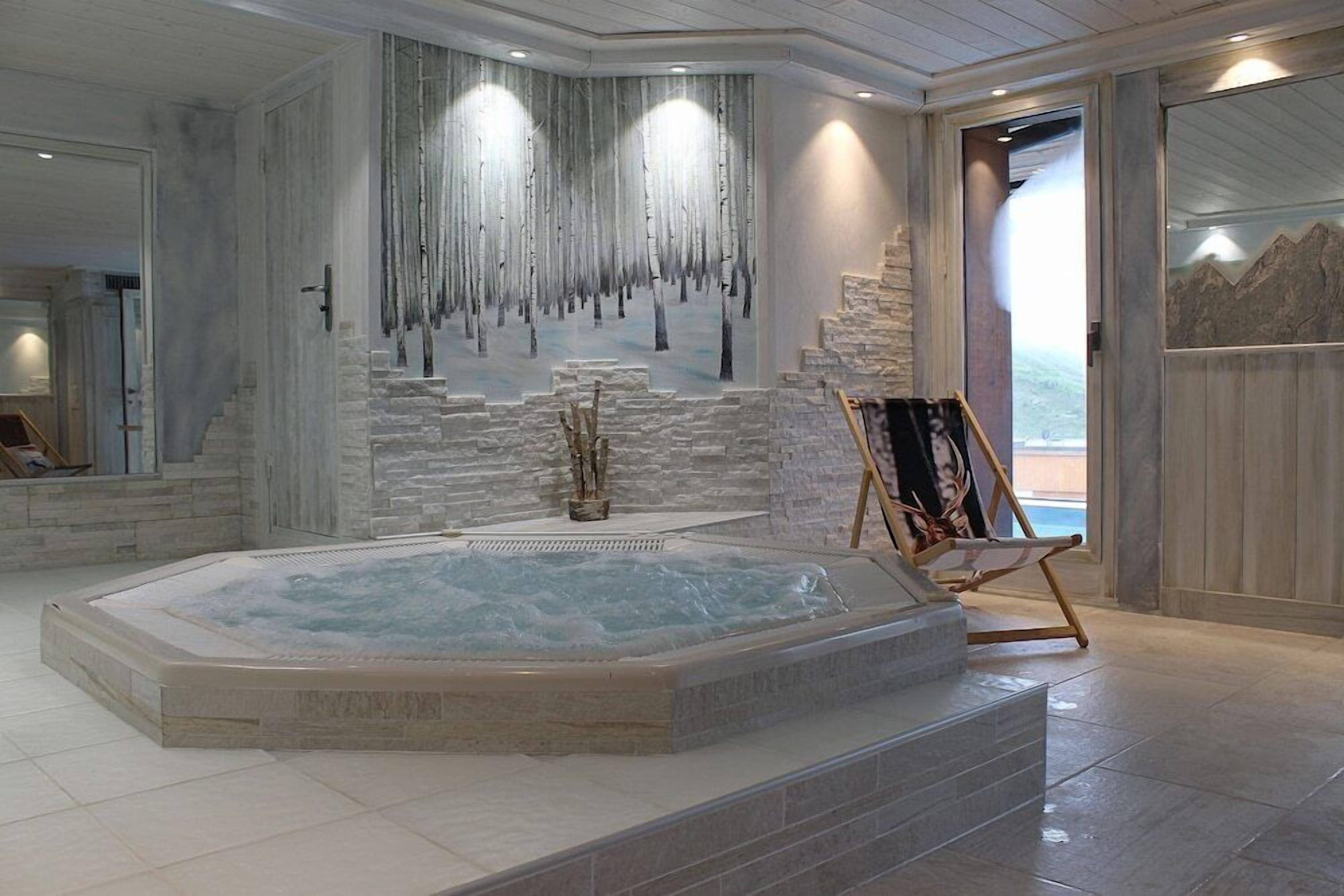 Un espace bien-être comprenant un jacuzzi, des murs en pierre et une terrasse en bois.