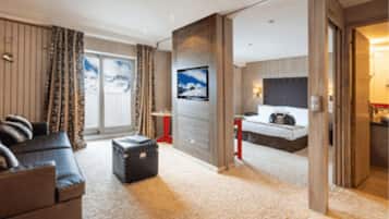 Une chambre d’hôtel dotée d’un grand lit, d’un coin salon avec un canapé et un pouf, d’une télévision et d’une porte coulissante donnant accès à la salle de bain.