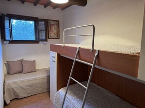 Un llit superposat amb una escala, un llit individual, una finestra i un quadre al mur.