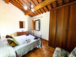 A bedroom with a bed, wooden wardrobe, and a window with a mirror. - Podere Di Mero Casolare by Interhome (Buti)