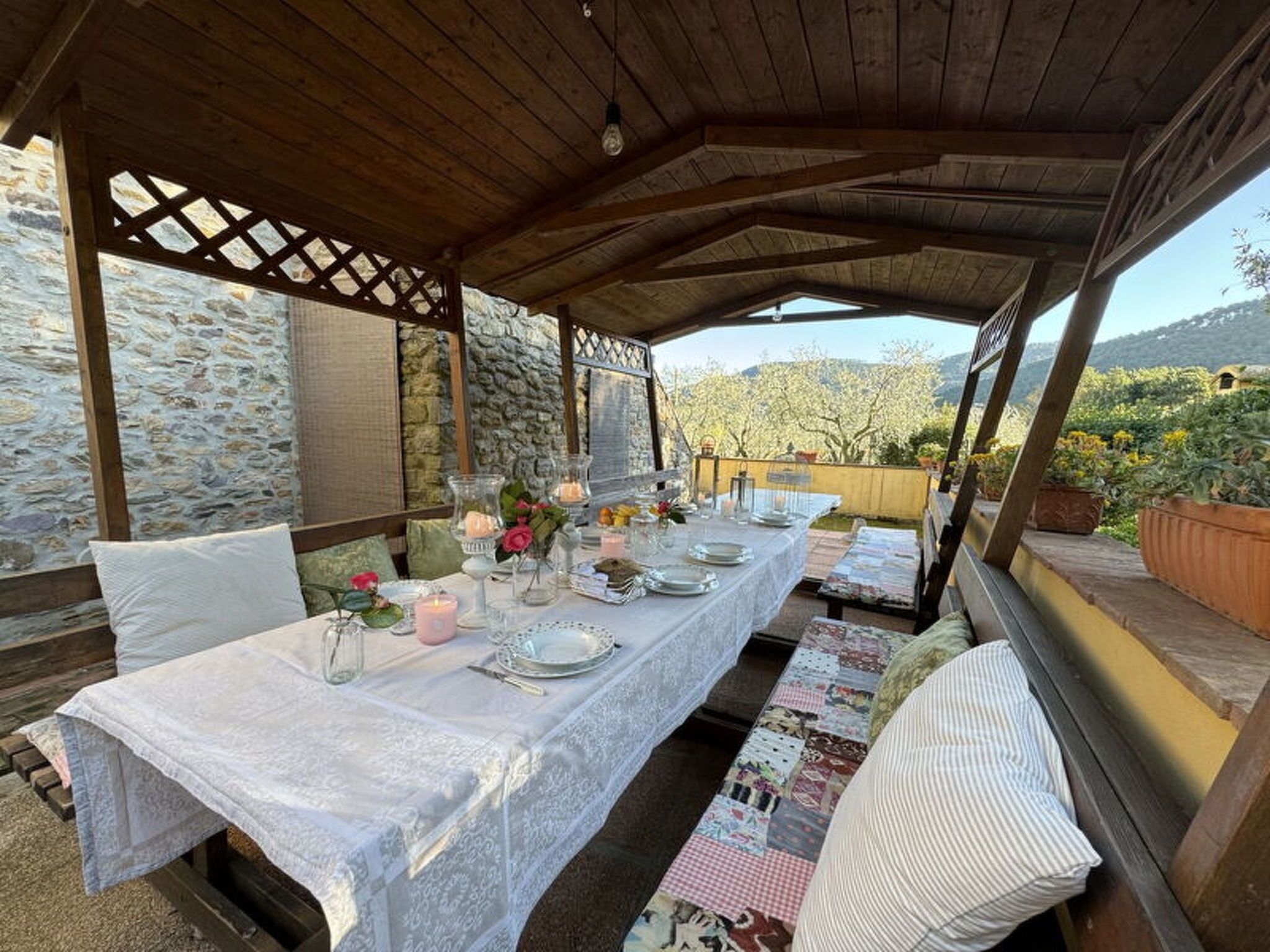 Un espace de restauration extérieur abrité, avec des murs en pierre, une table dressée pour deux personnes et une vue sur la campagne.