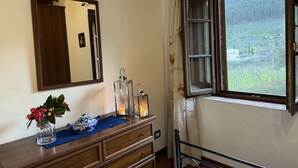 A bedroom with a wooden dresser, a mirror, a window with a view of a vineyard, and a bed with a metal frame. - Podere Di Mero Casolare by Interhome (Buti)