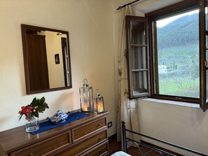 A bedroom with a wooden dresser, a mirror, a window with a view of a vineyard, and a bed with a metal frame. - Podere Di Mero Casolare by Interhome (Buti)