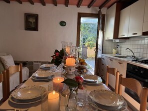 Taula de dinar per a quatre amb espelmes, un vas amb flors i vista al jardí a través d'una porta oberta.