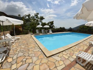 Una piscina amb rajoles de pedra, gandules blanques i para-sols.
