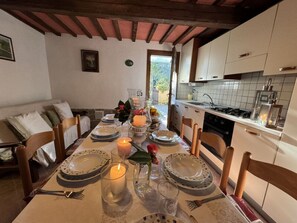 A dining table set with plates, glasses, and a candle, with a kitchen in the background. - Podere Di Mero Casolare by Interhome (Buti)
