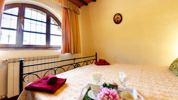 A bedroom with a bed, a window with curtains, a radiator, and a tray with a flower and cups on the bed. - Podere Di Mero Casolare by Interhome (Buti)