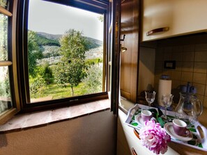 A window with a view of a green landscape, a table with a tray, a vase of flowers, and a candle. - Podere Di Mero Casolare by Interhome (Buti)