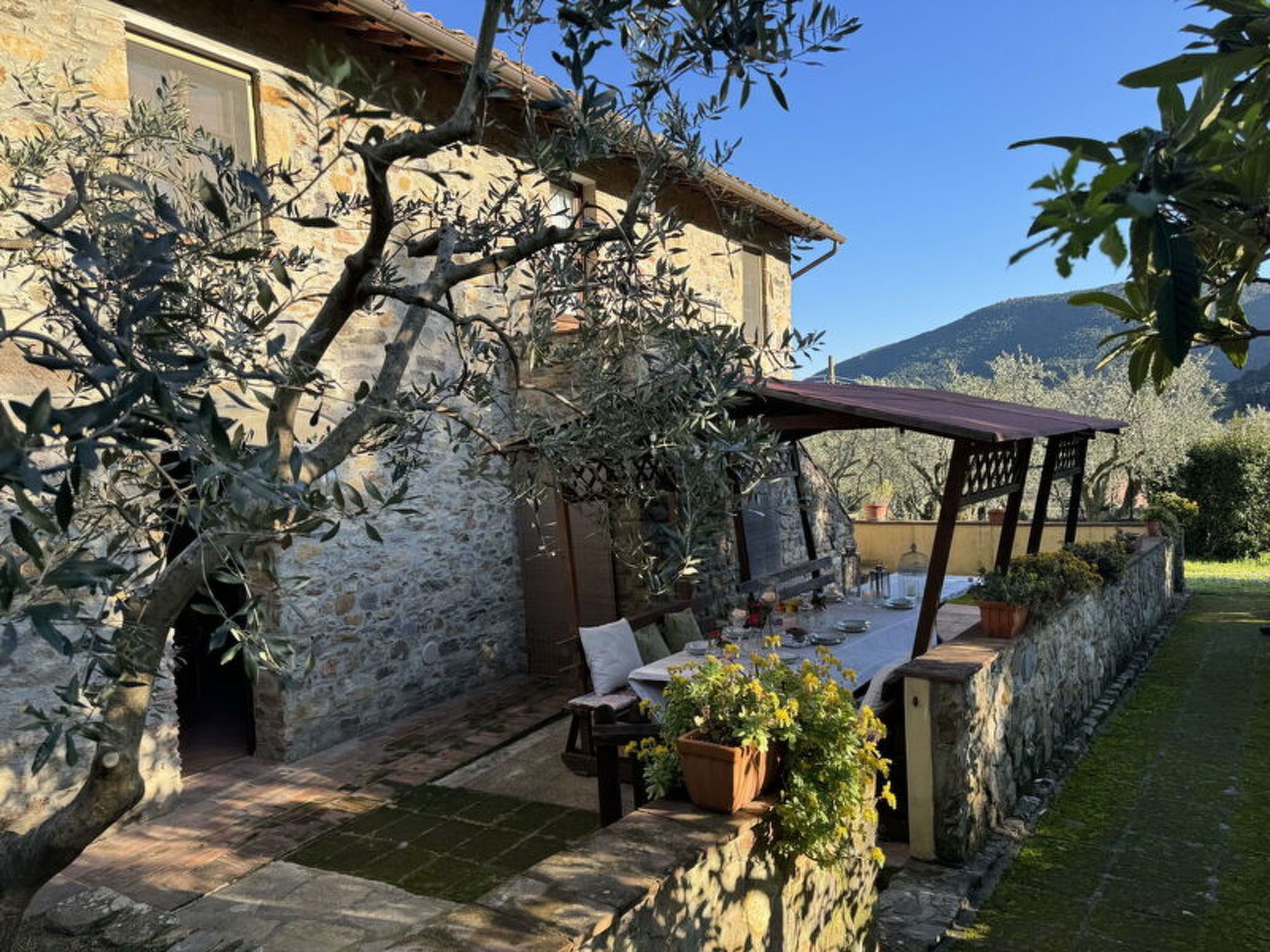 A stone building with a covered outdoor seating area, potted plants, and a view of the surrounding landscape.