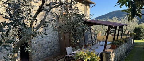 A stone building with a covered outdoor seating area, potted plants, and a view of the surrounding landscape.