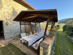 A stone building with a covered outdoor dining area, a table set for two, and a view of a garden and mountains. - Podere Di Mero Casolare by Interhome (Buti)