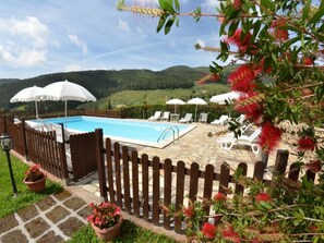 A pool area with a wooden fence, lounge chairs, and umbrellas. - Podere Di Mero Casolare by Interhome (Buti)