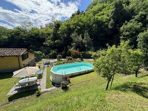 A swimming pool surrounded by a grassy area, a small patio with chairs, and a building with a tiled roof. - Casa Milena by Interhome (La Sassa)