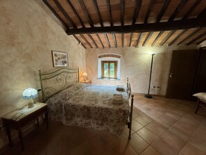 Ein Schlafzimmer mit Bett, Nachttisch, Lampe, Fenster und Tür.