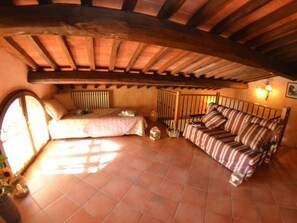 A cozy room with a bed, a striped sofa, a small table, and a staircase. - Casa Milena by Interhome (La Sassa)