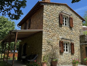 Ein Steinhaus mit einer Veranda, Holzklappläden und Blumentöpfen.