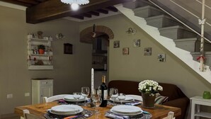 A dining area with a wooden table set for four, a staircase, and a small side table with a vase of flowers. - Anfora!! by Interhome (Pescia)