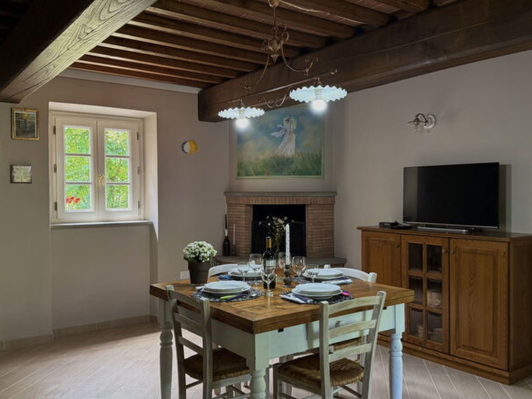 Un coin repas avec une table en bois dressée pour quatre personnes, une cheminée et un téléviseur posé sur un meuble.