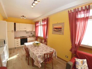 A dining area with a table set for four, a kitchen with white cabinets, and a red sofa. - Borgo Di Zacco by Interhome (La Sassa)