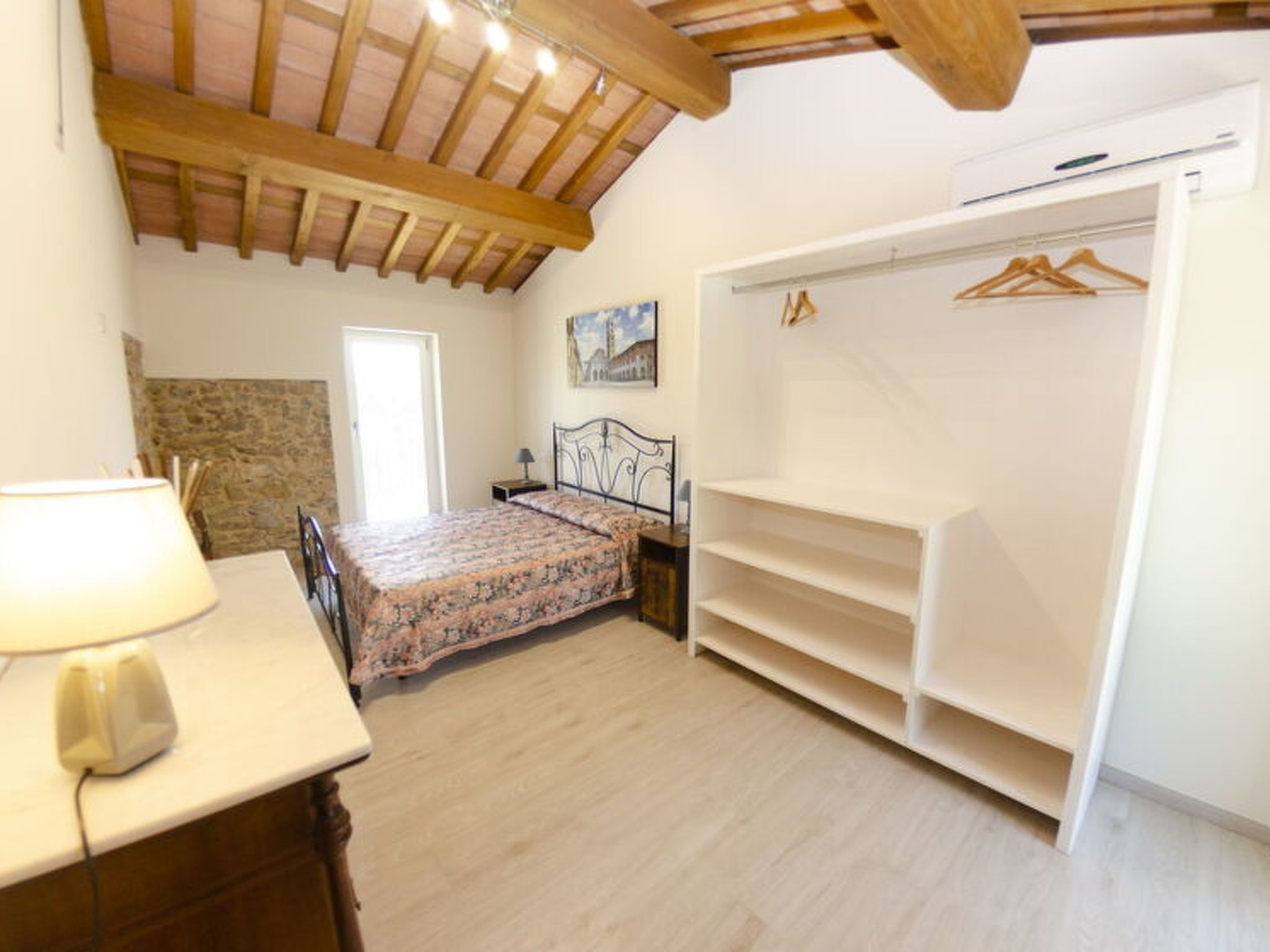 Une chambre à coucher avec un lit, une table de chevet, une lampe, une armoire et un tableau au mur.
