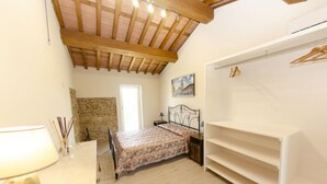 Un dormitorio con cama, armario, escritorio con lámpara, pared de piedra y un cuadro en la pared.