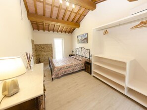 Ein Schlafzimmer mit Bett, Kleiderschrank, Schreibtisch mit Lampe, Steinwand und einem Gemälde an der Wand.