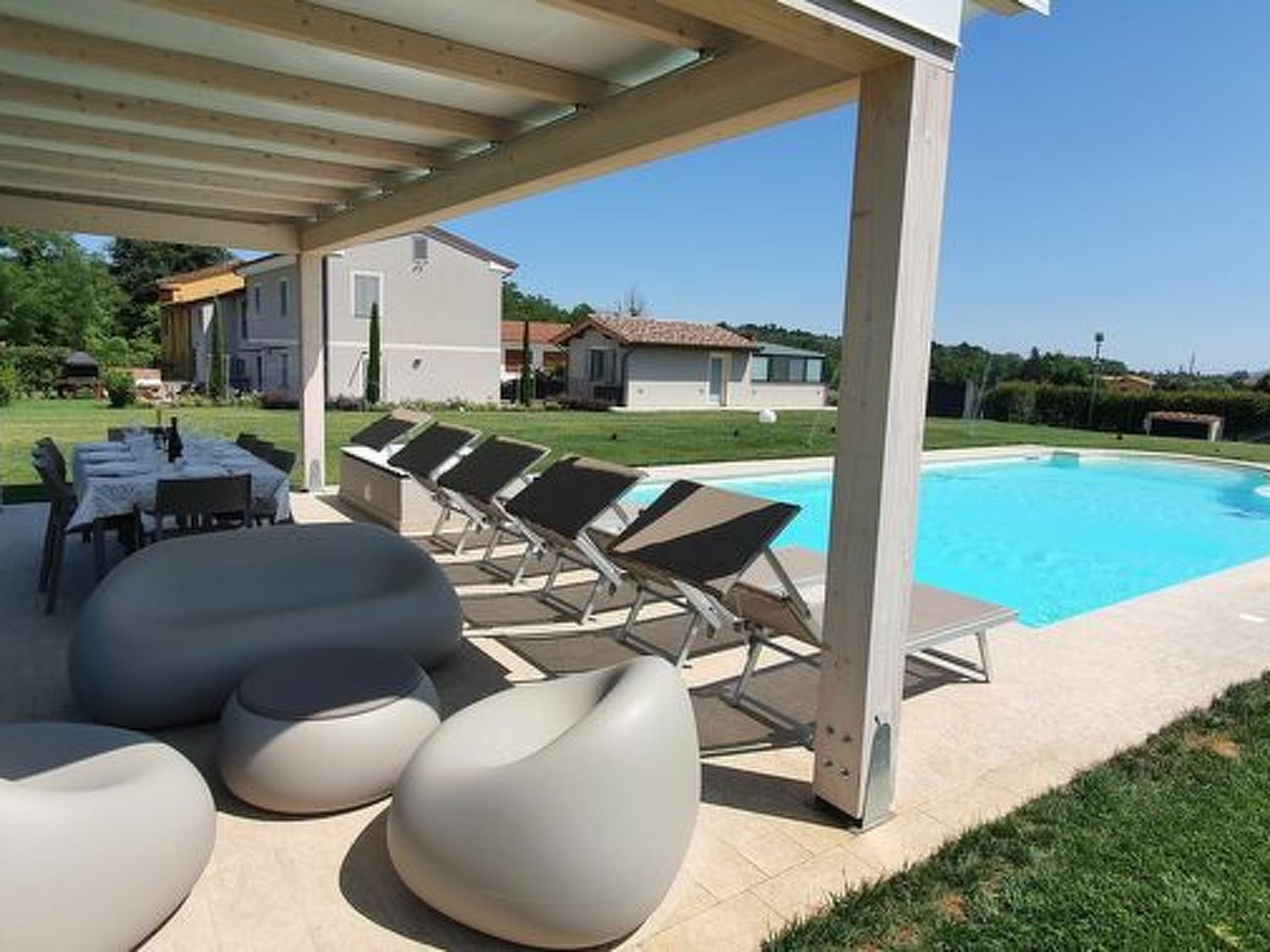 A covered outdoor area with a pool, lounge chairs, and a table with chairs.